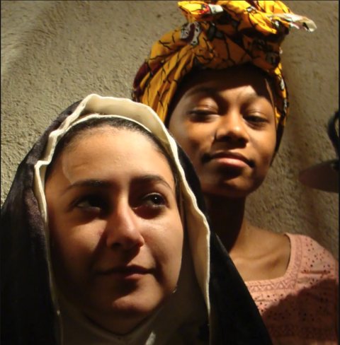 一个修女的特写镜头，她站在一个裹着头巾的女孩旁边，微笑着看着她.  