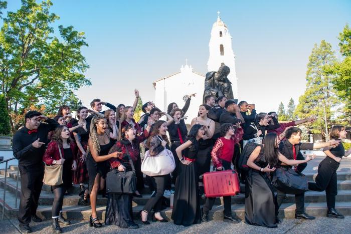 2024年在德拉萨雕像前的合唱团照片，拿着手提箱，看着左边
