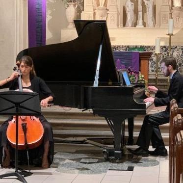 两个音乐家，一个在弹钢琴，另一个在演奏立式弦乐器，在教堂里表演