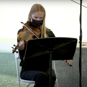 在新冠肺炎大流行期间，戴着黑色口罩的小提琴手. 她正在从乐谱架上读乐谱