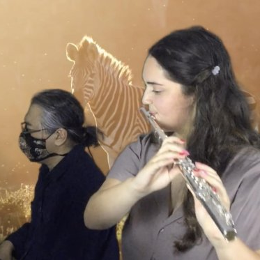 一个戴着面具的学生在利诺旁边吹长笛，弹钢琴. 有一个斑马的叠加背景. 