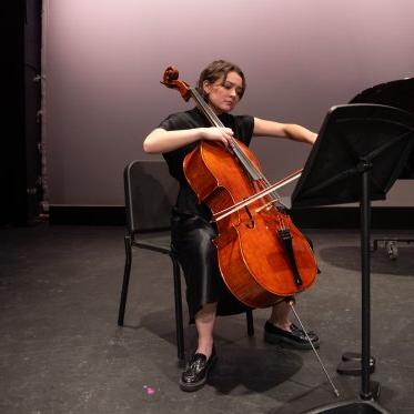 德西蕾·斯特罗克演奏大提琴的中号镜头, 在勒费夫尔剧院的舞台上，他看起来很专注. 她是在一个没有投影的背景下从上方被照亮的