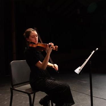 一位小提琴手在演奏她的乐器，看着她的乐谱架. 她独自坐在勒费夫尔剧院的舞台上，我们向座位区望去. 