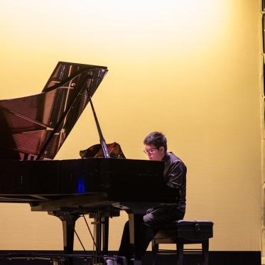 在勒费夫尔剧院，一名男钢琴手在柔黄色背景下的舞台上现场表演