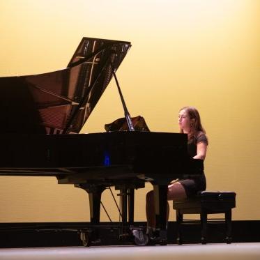 在勒费夫尔剧院，一名女钢琴演奏家在柔和的黄色背景下表演