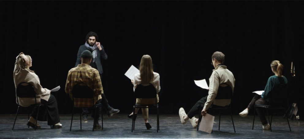 一位戏剧教授在舞台上对一群戏剧学生讲话