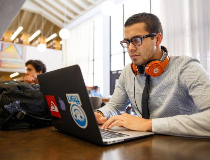 A student with headphones on working at a laptop in the library