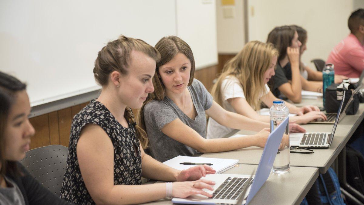 两个学生在课堂上看着一个笔记本电脑屏幕
