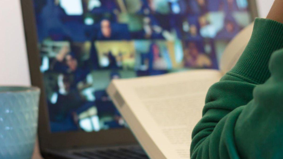 一个女人坐在电脑前看书，屏幕上显示着在线课程